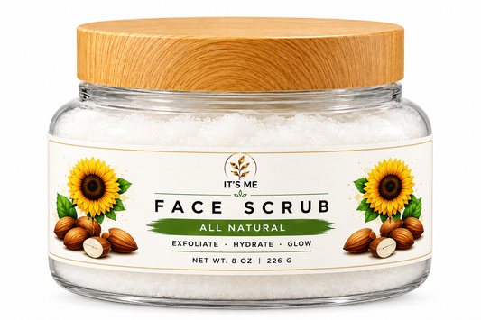 A clear glass jar of It's Me Face Scrub with a light wood lid, containing white exfoliating scrub. The front label features illustrations of sunflowers, almonds, and olives, with text reading 'FACE SCRUB ALL NATURAL'.
