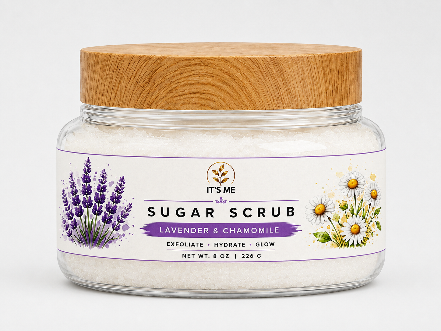A jar of 'It's Me' Sugar Scrub with lavender and chamomile, featuring white sugar crystals inside a clear glass jar with a light wood lid and a white label with purple and green illustrations.