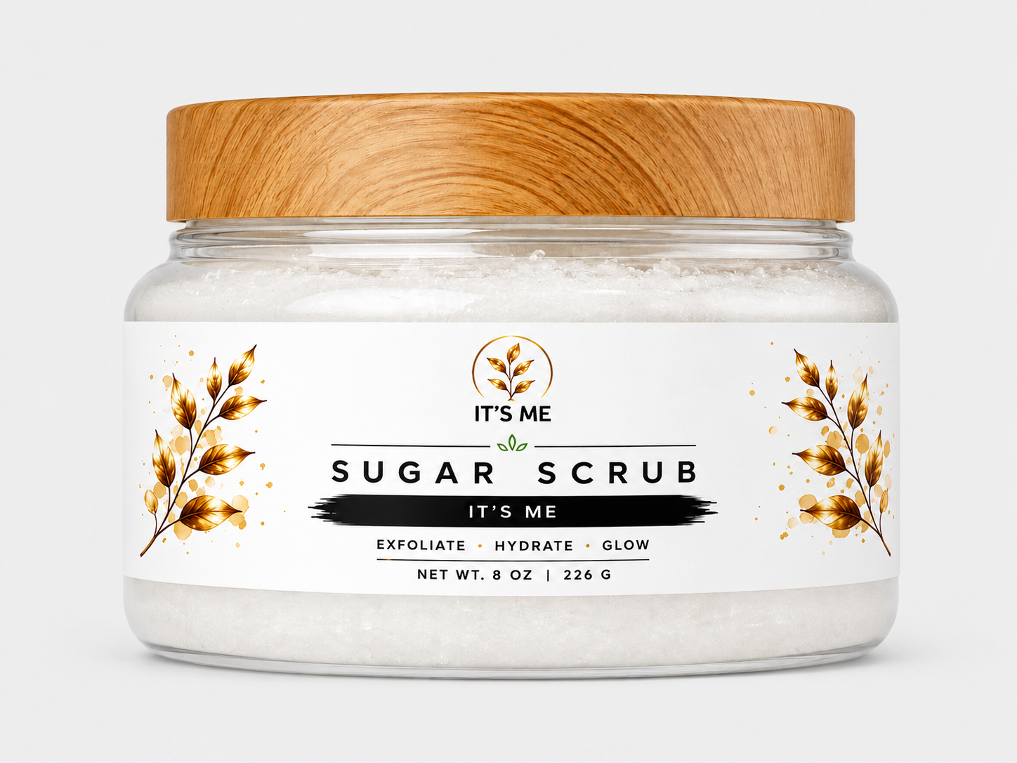 A jar of IT'S ME Sugar Scrub with a light brown wooden lid and a white label featuring gold botanical illustrations, set against a plain light gray background.